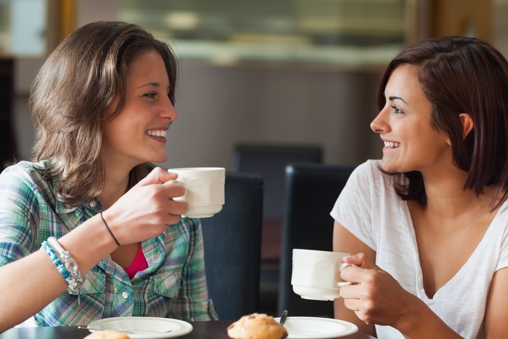 Two smiling students having a cup of coffee in college canteen